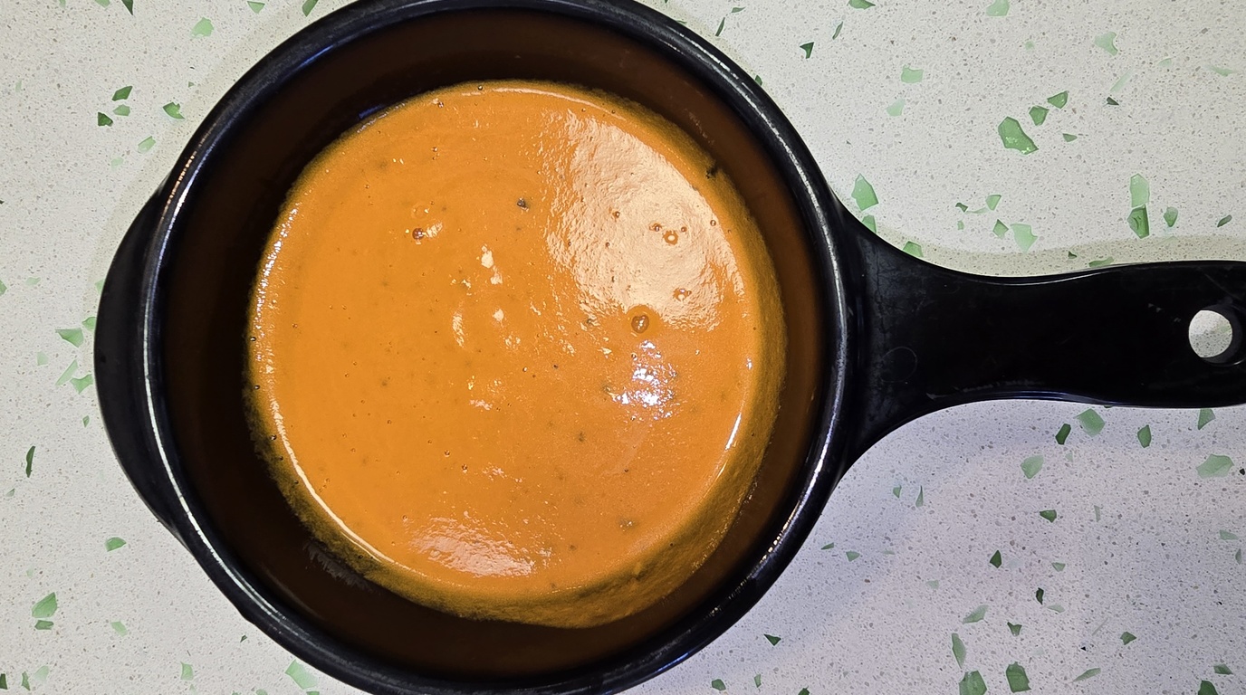 Ultra close-up macro food photography of rich velvety roasted tomato basil soup garnished with cream swirl, parmesan, and fresh basil